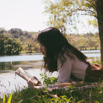 낮에 사진을 찍는 동안 책을 읽고 풀밭에 누워있는 여자.